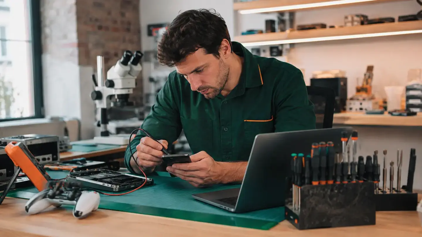 Device repair advice from Bristol technicians Professional Bristol electronics technician diagnosing a phone beside a MacBook and games controller